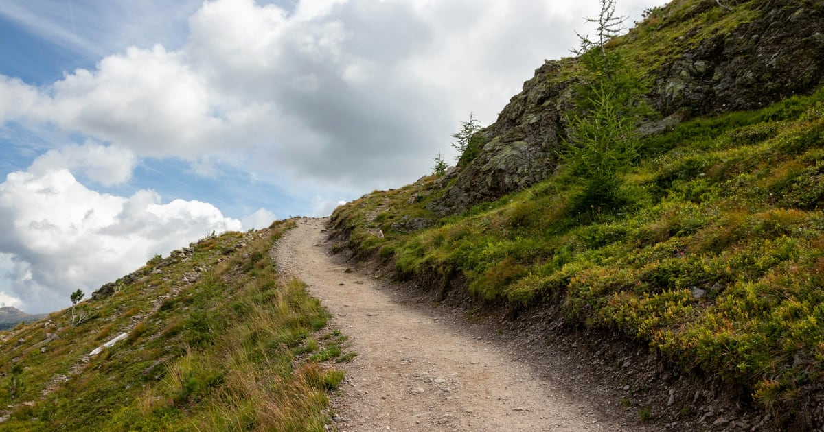 A footpath dipping between grassy slopes before climbing a hill under a cloudy sky