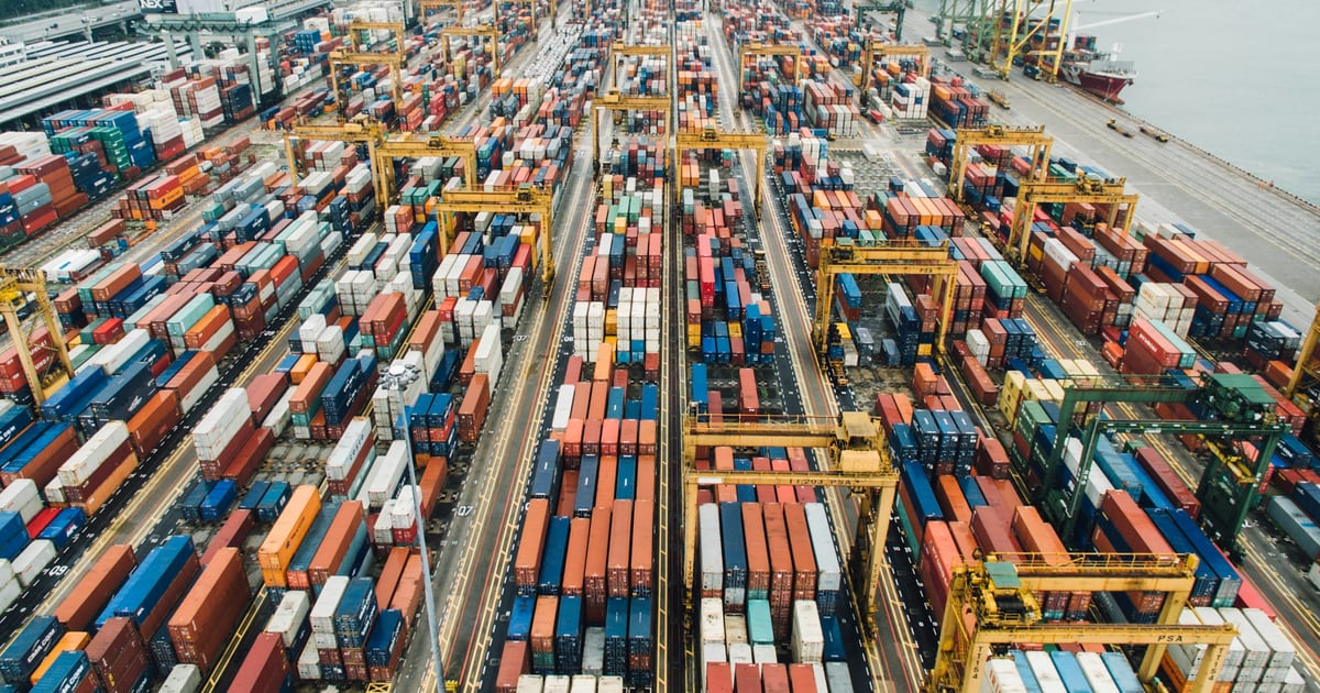 Aerial view of a container port with long rows of stacked shipping containers and gantry cranes