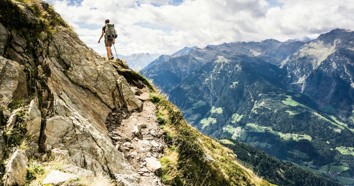 A hiker standing at the top of a steep rocky trail that drops toward a mountain valley