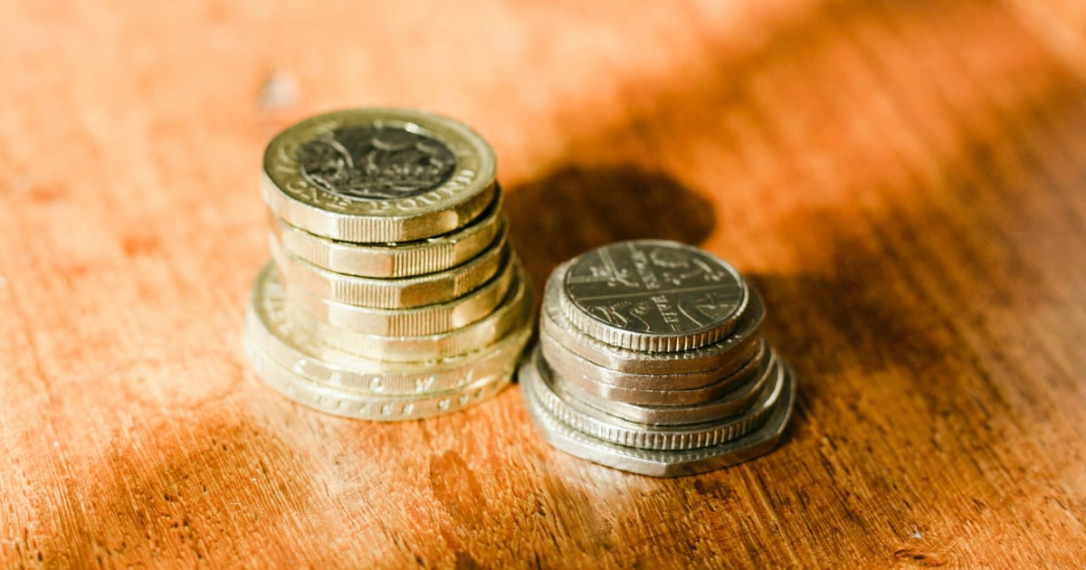 Two short stacks of silver and gold coins on a wooden table in warm side light
