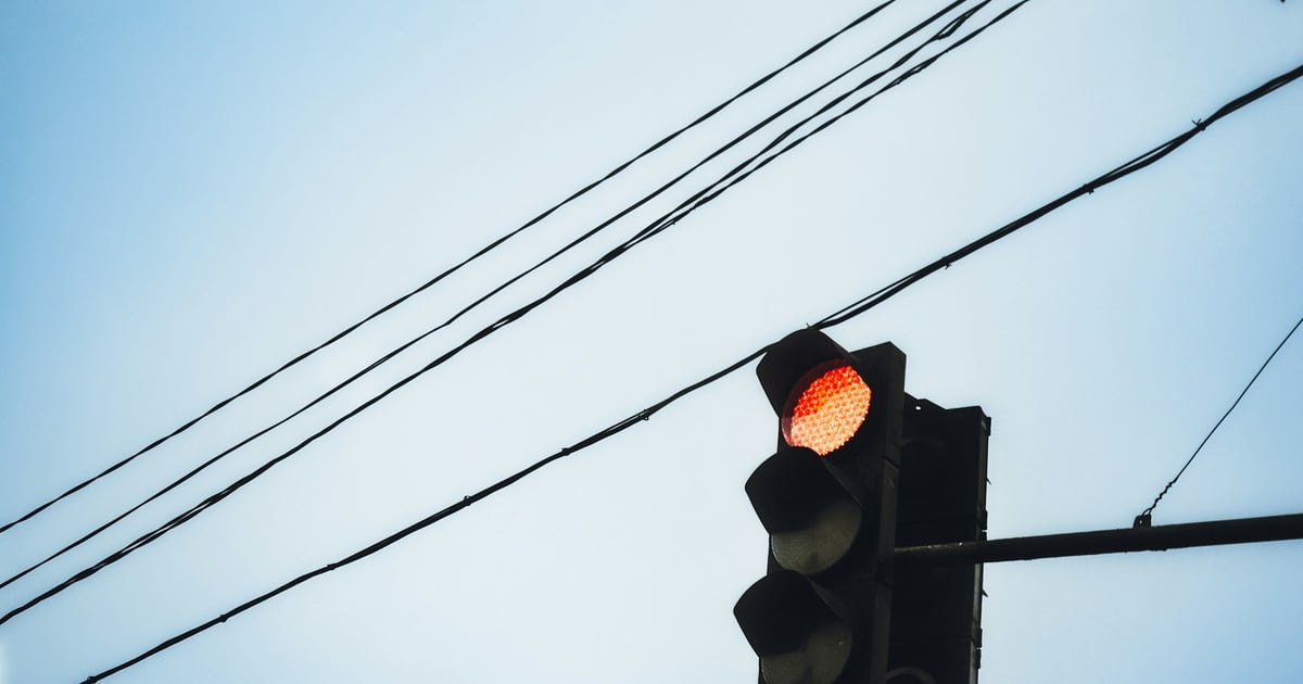 A traffic signal showing red, hanging from overhead wires against a pale sky