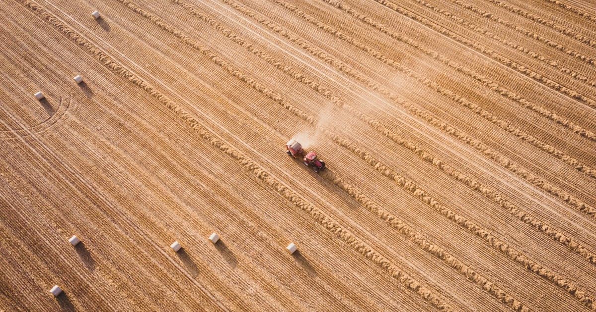 Aerial view of a harvested field with a tractor and scattered hay bales
