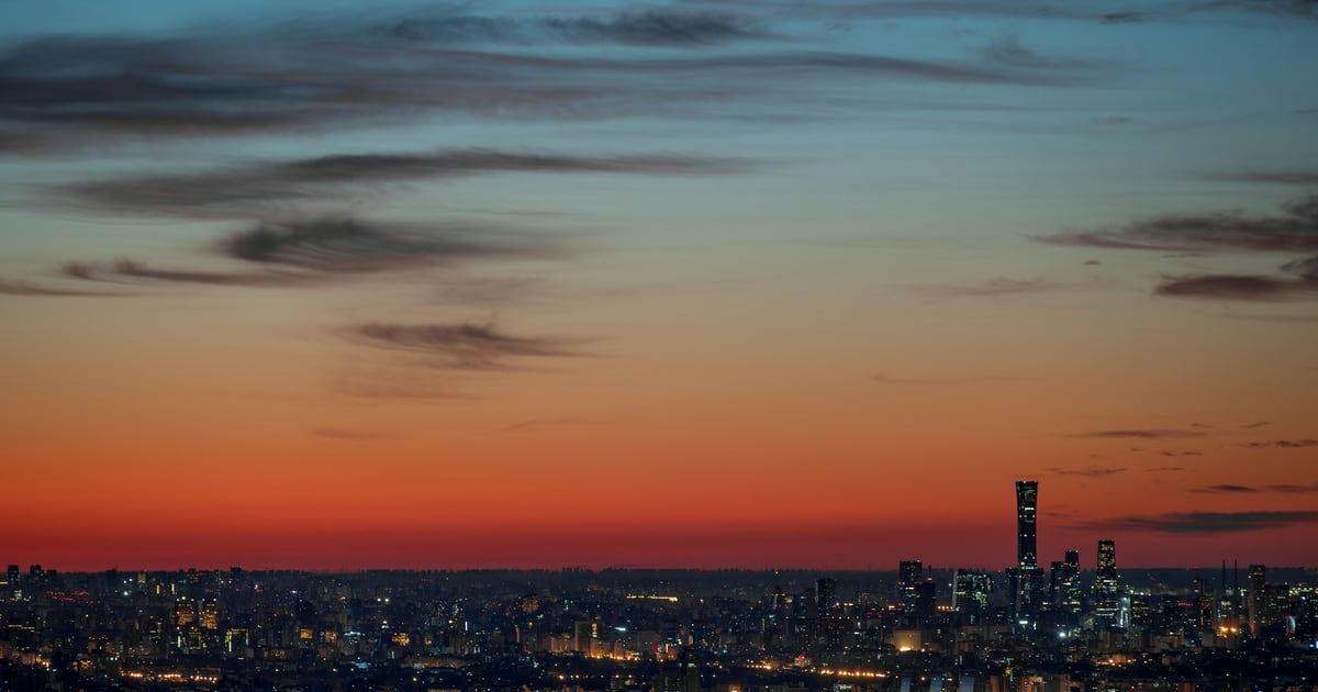 A city skyline in silhouette under an orange band of sky at dusk