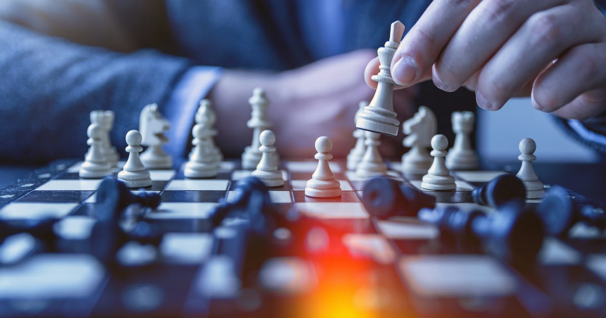 A hand moving a white chess piece forward during a game on a blue-lit board