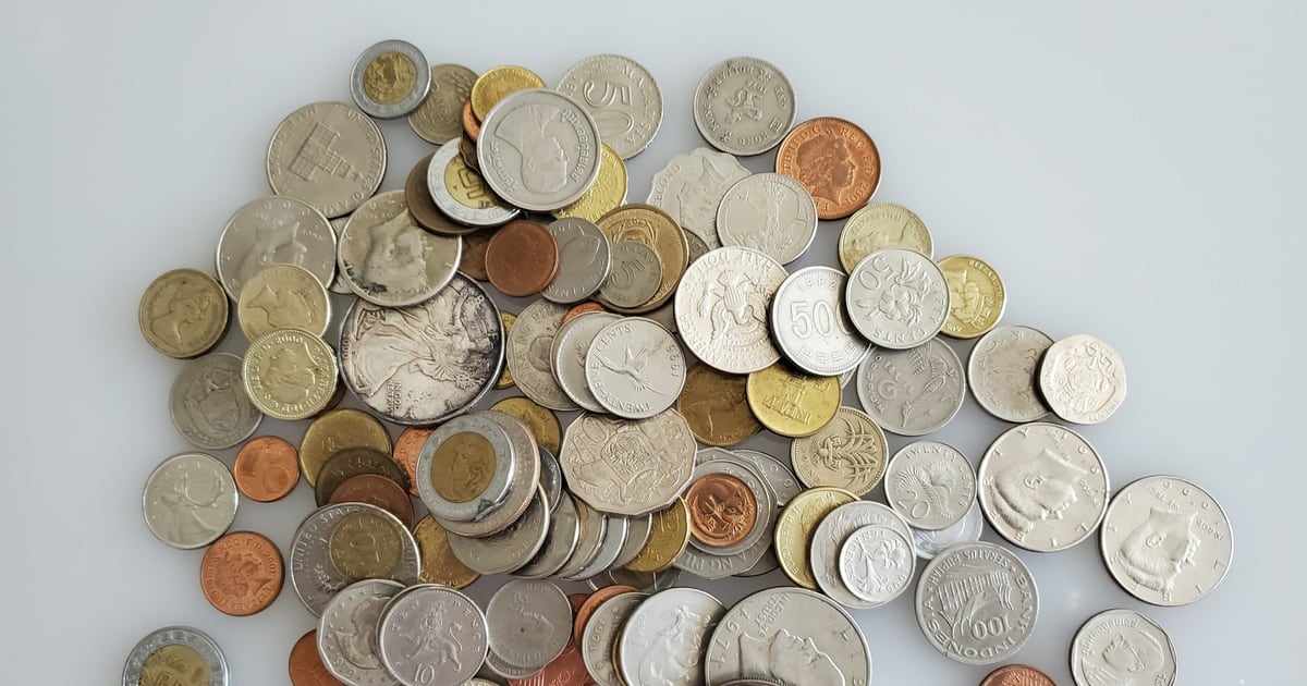 A pile of coins from many different countries on a white surface