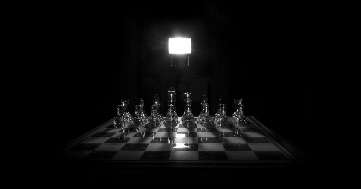 A chessboard in darkness with every piece lit by one overhead lamp